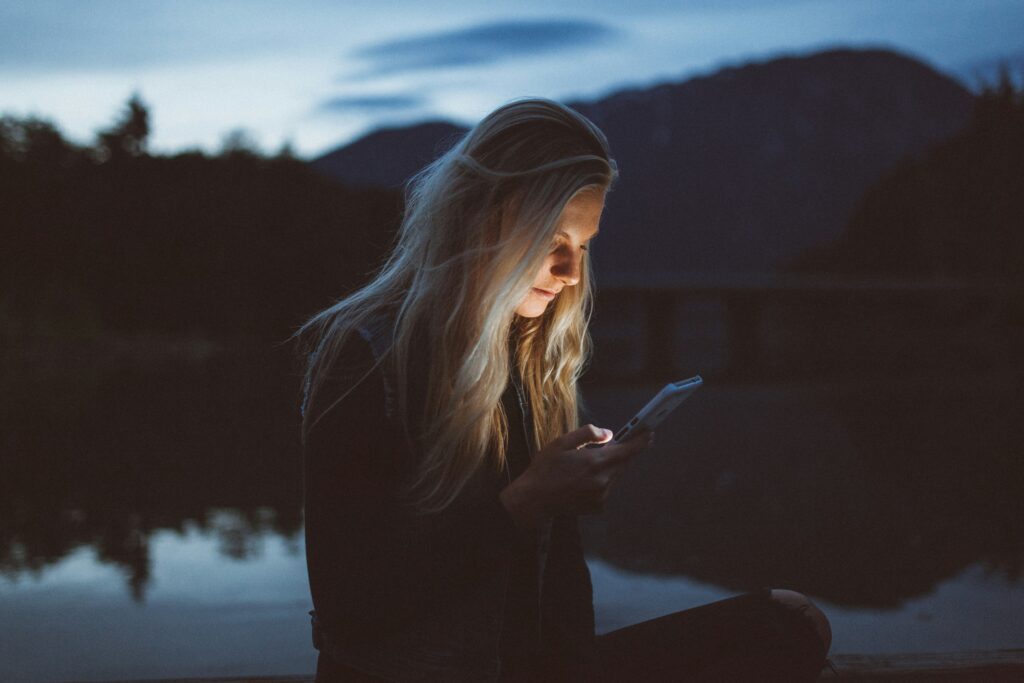 Woman typing into her phone at night by a lake, suggesting she is giving words to encourage a friend